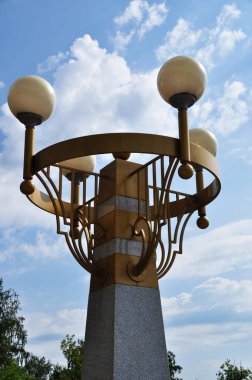 Şehir parkında aydınlatma direği. Mavi bir yaz gökyüzüne karşı bir fenerin yuvarlak gölgeleri.