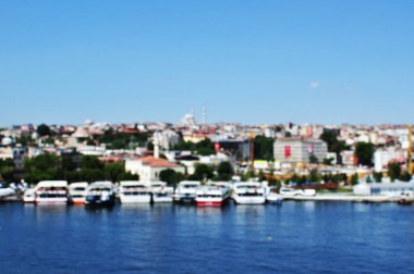 Odaklanamayan manzara. Suyun, şehir evlerinin ve açık mavi gökyüzünün odak noktası dışında. Bokeh.