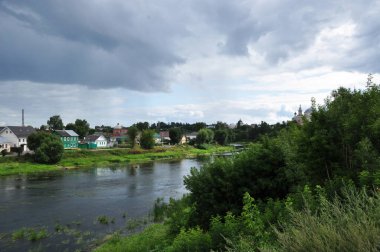 Tvertsa nehrinin panoramik manzarası. Nehir manzarası ve sahildeki ahşap evler. Yağmurdan önce bulutlar nehrin üzerinde süzülür..