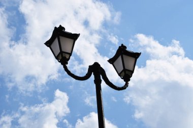 İki lambalı bir sütun. Gökyüzünde beyaz bulutlu bir lamba direği.