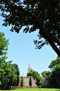 Parkın panoramik manzarası. Taşlarından yüksek bir duvarın arkasında sivri uçlu bir kule..