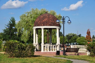 Parkta sütunları olan bir çardak. Bir çardağı, feneri ve bankı olan şehir parkının manzarası..