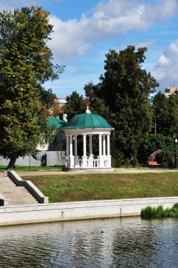 Parktaki yeşil çatının altında küçük bir çardak. Kanal ve beyaz taş merdiven manzarası.