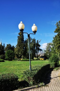 Şehir meydanı. Mavi gökyüzüne karşı yeşil ağaçlar ve fener manzarası.