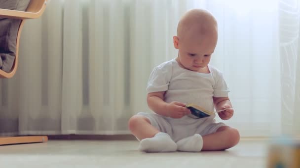 Babyjongen zittend op de vloer met boek — Stockvideo