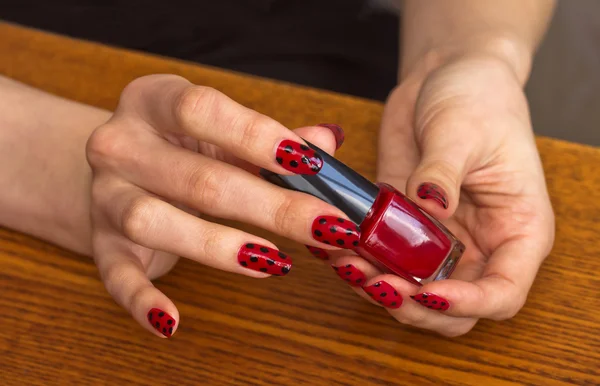 Manos de niña con esmalte de uñas rojo sosteniendo una botella con barniz — Foto de Stock