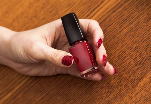 Mano femenina con manicura roja sosteniendo botella de esmalte de uñas — Foto de Stock