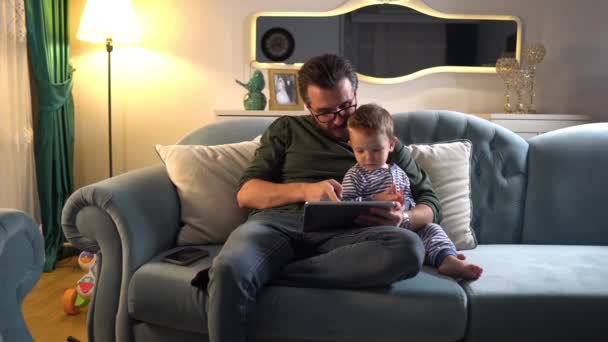 爸爸和可爱的男婴坐在沙发上 在家一起玩数码桌球 — 图库视频影像