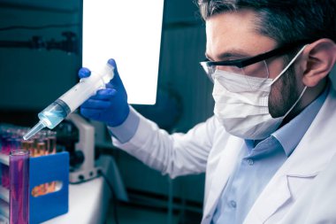 Laboratuvarda test tüplerini kontrol eden genç bir bilim adamı. Adam koruyucu gözlük takıyor.