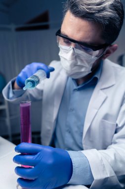 Laboratuvarda test tüplerini kontrol eden genç bir bilim adamı. Adam koruyucu gözlük takıyor.