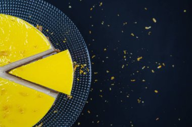 Siyah arka planda cam tabakta dilimlenmiş limonlu cheesecake. (Boşluk)