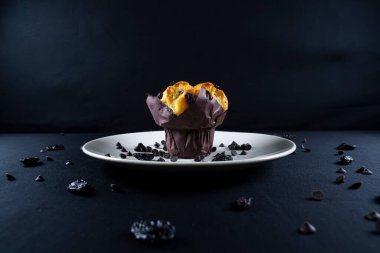 Çikolata, üzümlü cips ve beyaz tabakta kuru üzümlü kek. Siyah arka plan. Kopyalama alanı