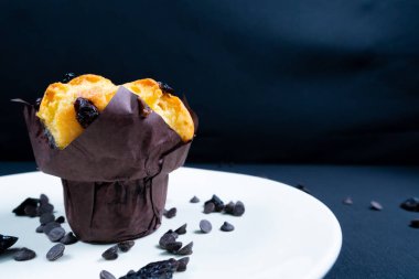 Çikolata, üzümlü cips ve beyaz tabakta kuru üzümlü kek. Siyah arka plan. Kopyalama alanı