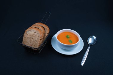 Fesleğenli domates çorbası ve kasede ekmek. Koyu arkaplan.