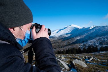 Dağdaki adam karla kaplı dağı fotoğraflıyor.