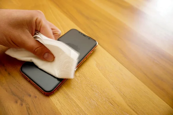 30 Nisan 2021 Eskisehir Türkiye. Adam ahşap masaya dezenfektan havluyla iPhone siliyor.
