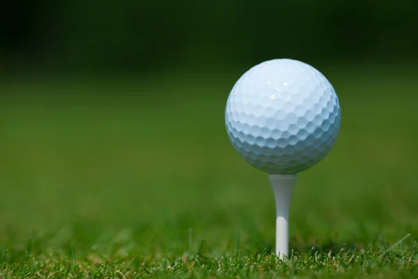Golfboll på en vit tee med ett grönt gräs i bakgrunden — Stockfoto