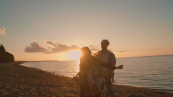 Pár běží a usmívá se na pláži při pohledu na krásný západ slunce — Stock video