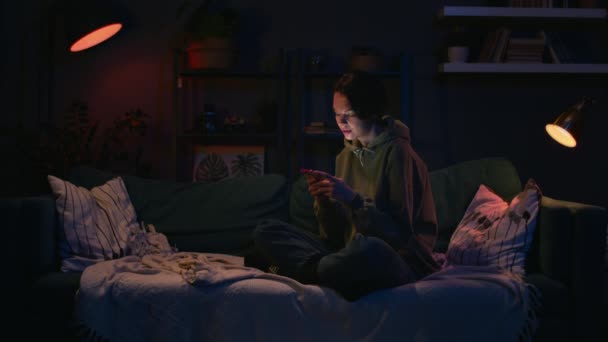 Dziewczyna rozmawiać z przyjaciółmi za pomocą telefonu, kobieta pracuje na kanapie wieczorem — Wideo stockowe