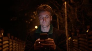  Yakışıklı genç adam akıllı telefonuyla yürüyor ve yazı yazıyor.