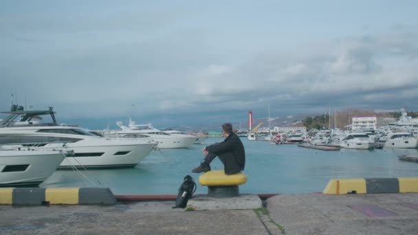 Чоловік сидить на пірсі і дивиться на море в сонячний день — стокове відео