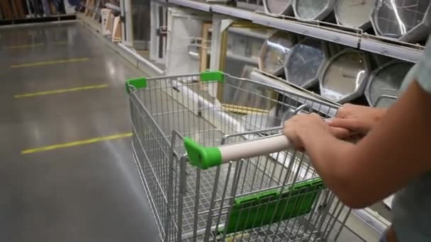 As mãos das mulheres empurram um carrinho de compras em um supermercado. Compras. Loja de construção, comprar para o interior. Venda. Descontos. — Vídeo de Stock