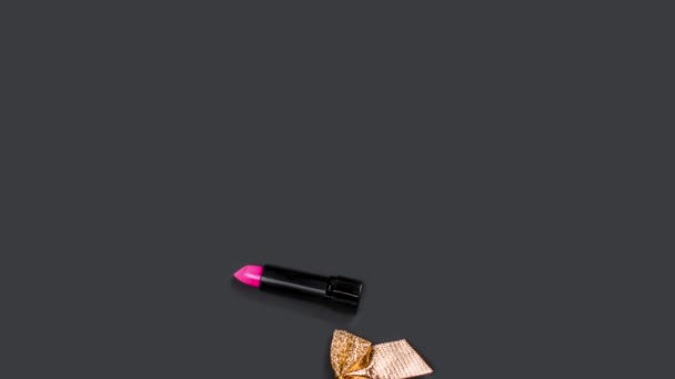 Accessori per il trucco rosa e oro appaiono e scompaiono su sfondo nero con coriandoli e fiocchi. Rossetto, smalto, siero, pennello rosso. Prodotti cosmetici per la cura del viso. Video in loop. Regali di Natale. — Video Stock