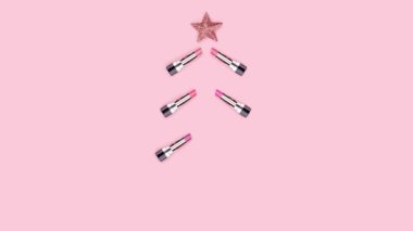 Renkli rujlardan yapılmış Noel ağacı, Noel baloları, pembe arka planda yıldızlar. Beauty Xmas konsepti. Makyaj malzemeleri. Kozmetik ürünler. Kırmızı, mor, dudak parlatıcısı. Hareketi durdur.