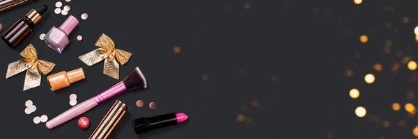 Aksesoris makeup merah muda dan emas di latar belakang hitam dengan lampu bokeh dan busur. Produk kosmetik untuk perawatan wajah. — Stok Foto