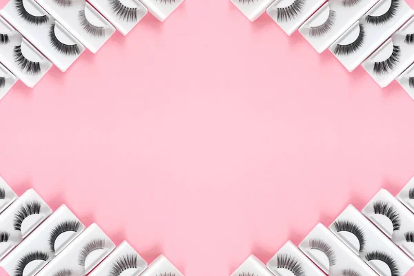 Renkli pastel pembe arka planda farklı takma kirpikleri var. Güzellik deseni. Makyaj malzemeleri. Kozmetik ürünleri.