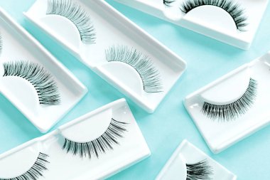 Mavi arka planda farklı takma kirpikleri var. Güzellik. Makyaj malzemeleri. Göz kirpikleri için kozmetik ürünler.