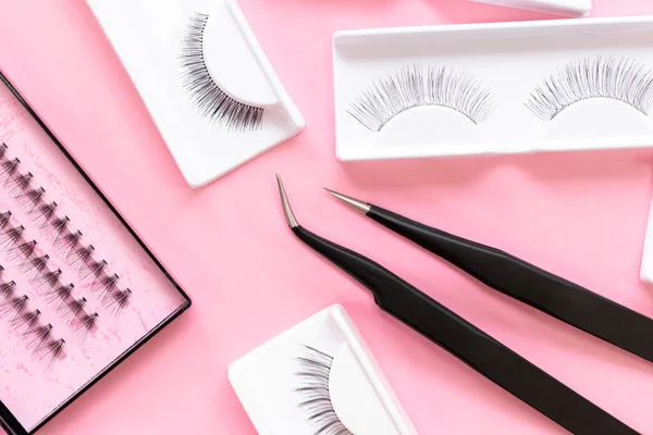Moda pastel pembe arka planda kirpik uzantıları için araçlar. Sahte kirpikler ve cımbızlar. Makyaj araçları.