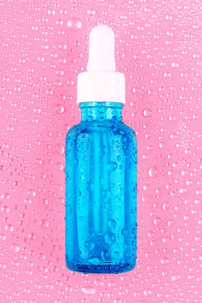 Cam şişedeki nemlendirici serum pembe arka planda beyaz pipet ve su damlaları. Hidrasyon için Hyaluronik asit