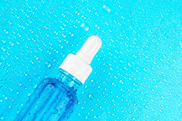 Cam şişedeki nemlendirici serum mavi arka planda beyaz pipet ve damlalar. Hidrasyon için Hyaluronik asit. 