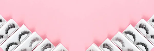 Different fake eyelashes on a trendy pastel pink background. Beauty pattern. Makeup accessories. Cosmetics products.