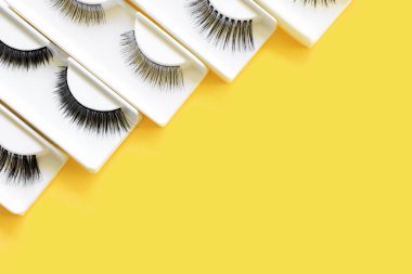Sarı arka planda farklı takma kirpikleri var. Güzellik deseni. Makyaj malzemeleri. Kozmetik ürünler. Aydınlatıcı.