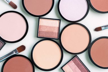 Mavi arka planda farklı bej rengi allık ve kompakt yüz pudraları. Göz farı paleti. Kozmetik ve makyaj fırçaları.