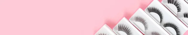 Different fake eyelashes on trendy pastel pink background. Beauty pattern. Makeup accessories. Cosmetic products. Banner