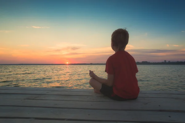 Young boy meditating on a pier — Stock Photo, Image