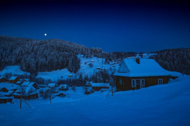 Karla kaplı Alp kış köyünün üzerinde ay batımı. Noel gecesi.