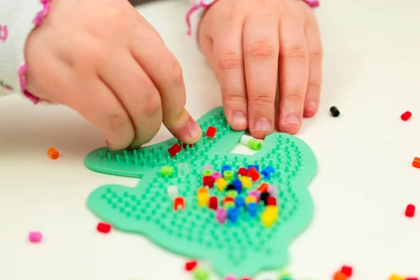 Development of fine motor skills in children. Hands are in the foreground. Closeup. The child puts together a plastic mosaic.
