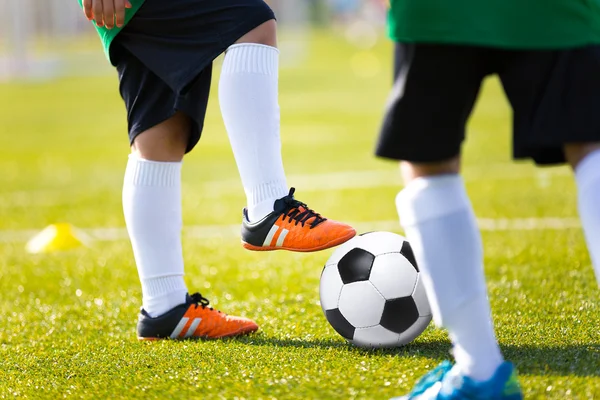 Legs feet of football player in white sports socks orange shoe and green shirt kicking soccer ball. Training session on green fresh grass for youth football soccer team.
