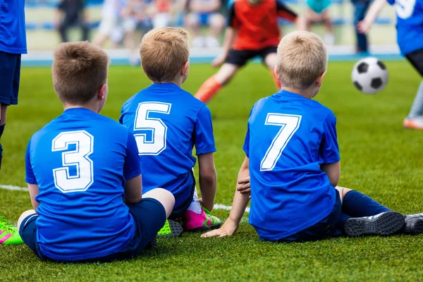 Giovane squadra di calcio. Riserva giocatori seduti insieme e guardare la partita dei tornei di calcio per le squadre giovanili . — Foto Stock