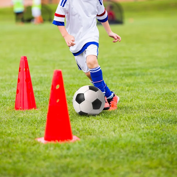 Un chico jugando al fútbol. Entrenamiento de fútbol para niños. Chicos está entrenando con pelota de fútbol y bolardos en el campo de hierba —  Fotos de Stock