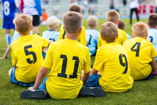 Детская футбольная команда на спортивном стадионе. Мальчики сидят на футбольном поле во время школьного футбольного турнира — стоковое фото