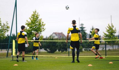 Genç futbolcular antrenman biriminde futbol oynuyorlar. Gençler çim sahada futbol antrenmanı yapıyor. Spor yapan genç çocuklar