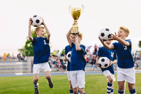 トーナメント決勝でサッカーの成功を祝う小学生のスポーツチームの幸せな男の子 サッカーの試合に勝つ子供たち 幸せな子供スポーツチームは黄金のトロフィーを上げ — ストック写真