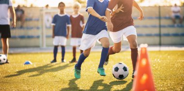 Küçükler futbol takımındaki çocukların portresi. Güneşli bir günde antrenman sırasında külahlar arasında top oynuyorlar. Okul gençleri sahada futbol antrenmanında.