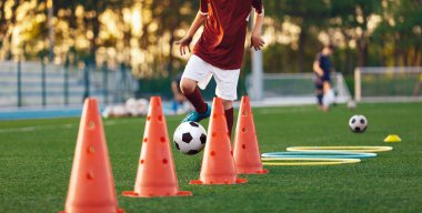 Çocuklar antrenman külahları arasında futbol topları koşuyor. Genç sporcular için Avrupa futbol yaz kampı. Sahada topları olan futbolcular. Arka planda futbol golü ve stadyum
