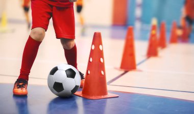 Çocuklar için futbol futsal eğitimi. Futbol antrenmanı külah tatbikatı. Spor salonunda futbol topuyla oynayan genç futbolcu. Mavi üniformalı bir oyuncu. Spor arkaplanı
